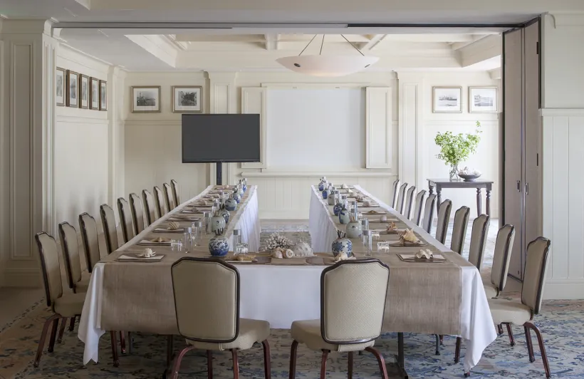 Conference room with long table, plants, projector and elegant decor in soft tones.