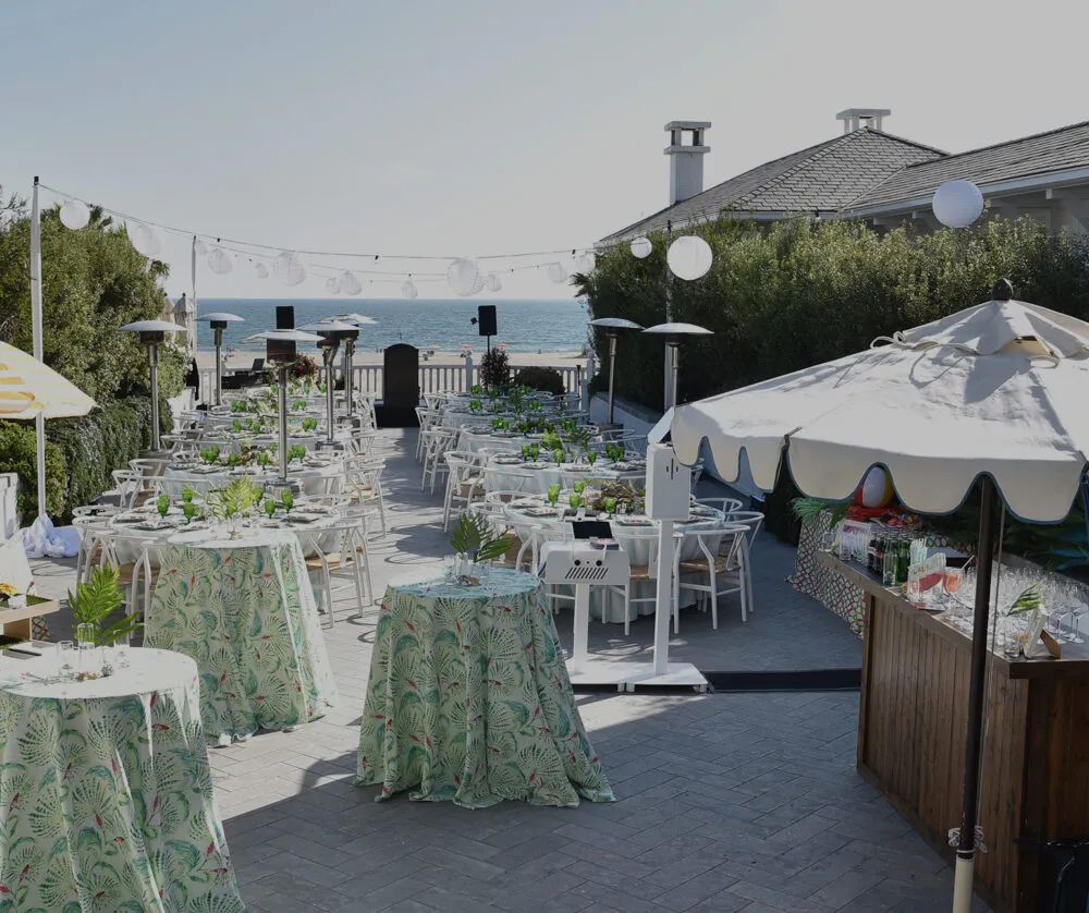 Chic outdoor event setup with tropical decor, ocean views, and string lights.