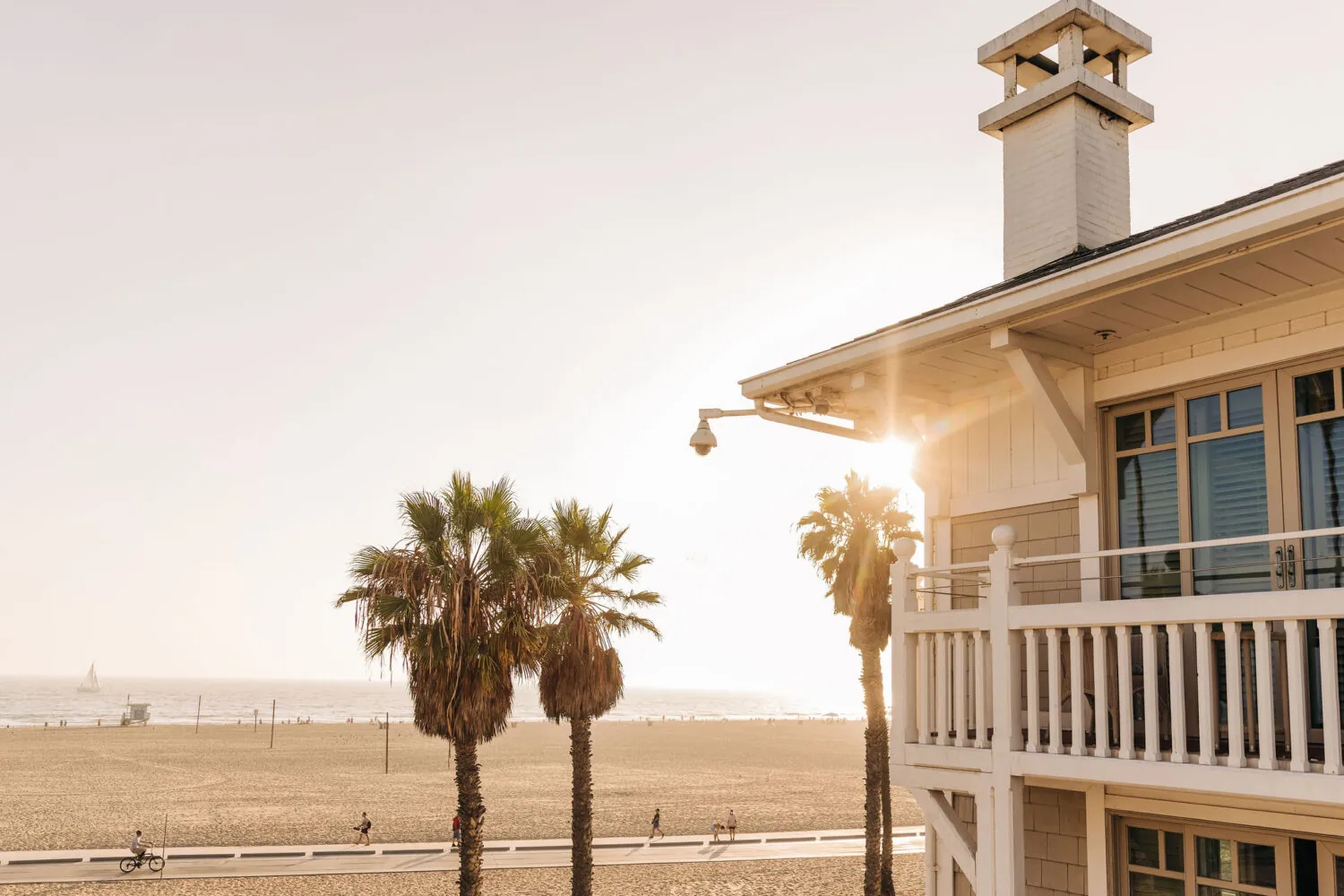 Beachfront sunset with palm trees, sand, and a coastal balcony.