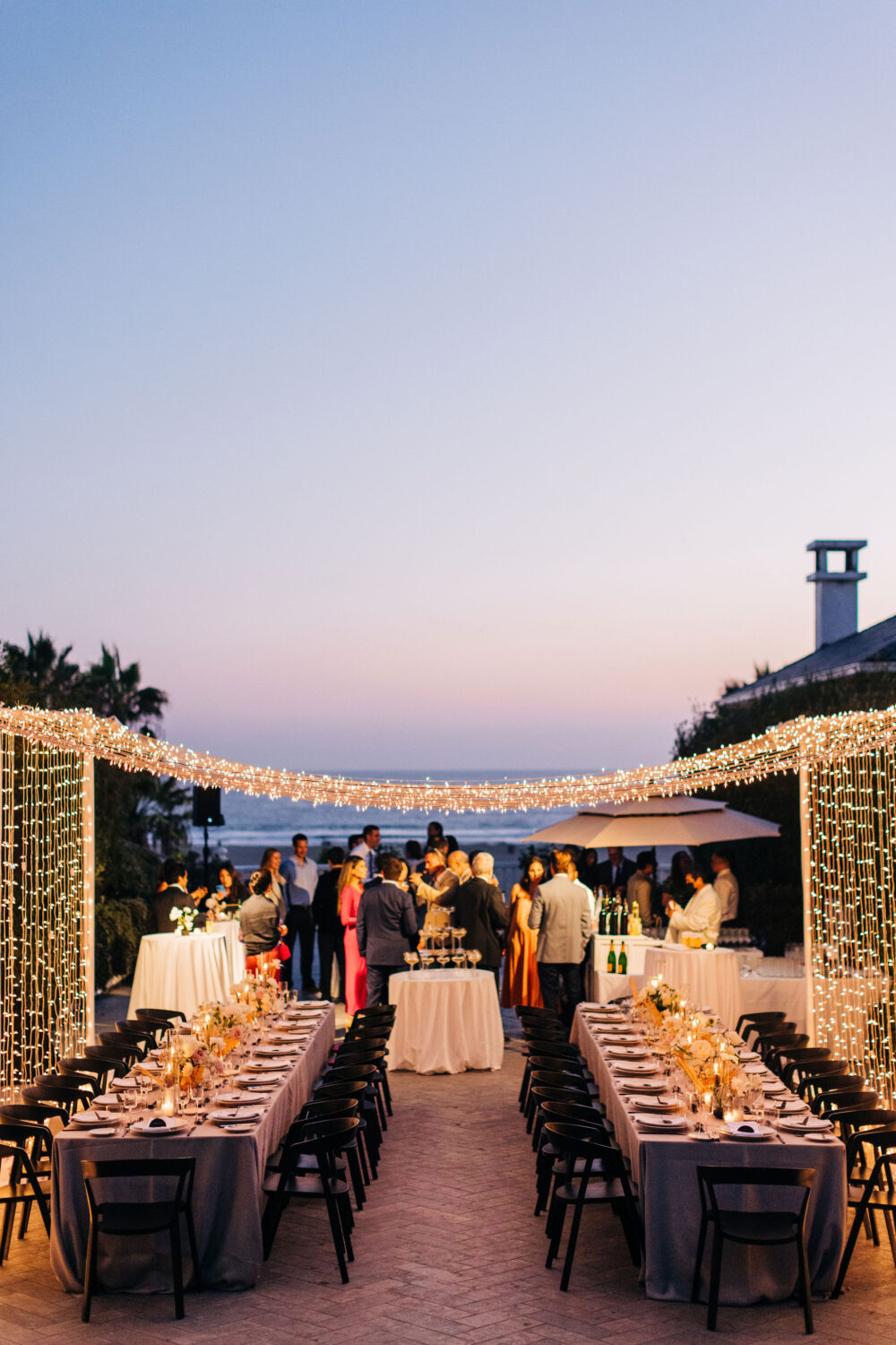 Outdoor evening wedding reception with string lights, long tables, and guests socializing.