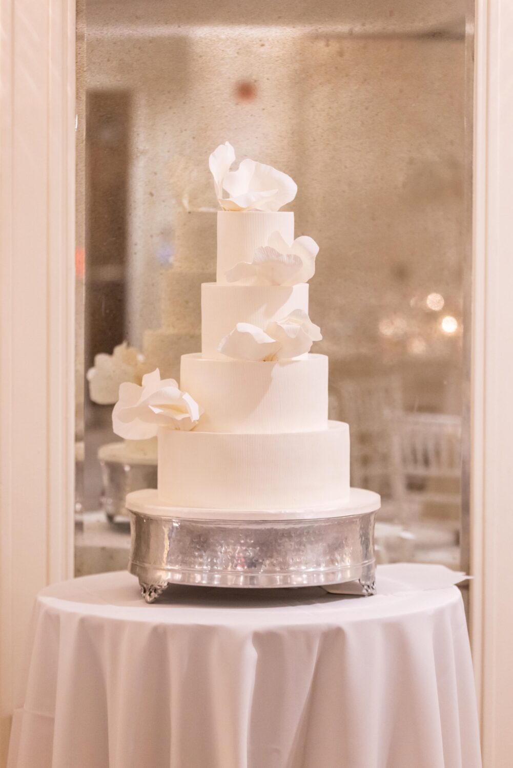 Elegant four-tier white wedding cake with delicate sugar flowers on a silver stand.