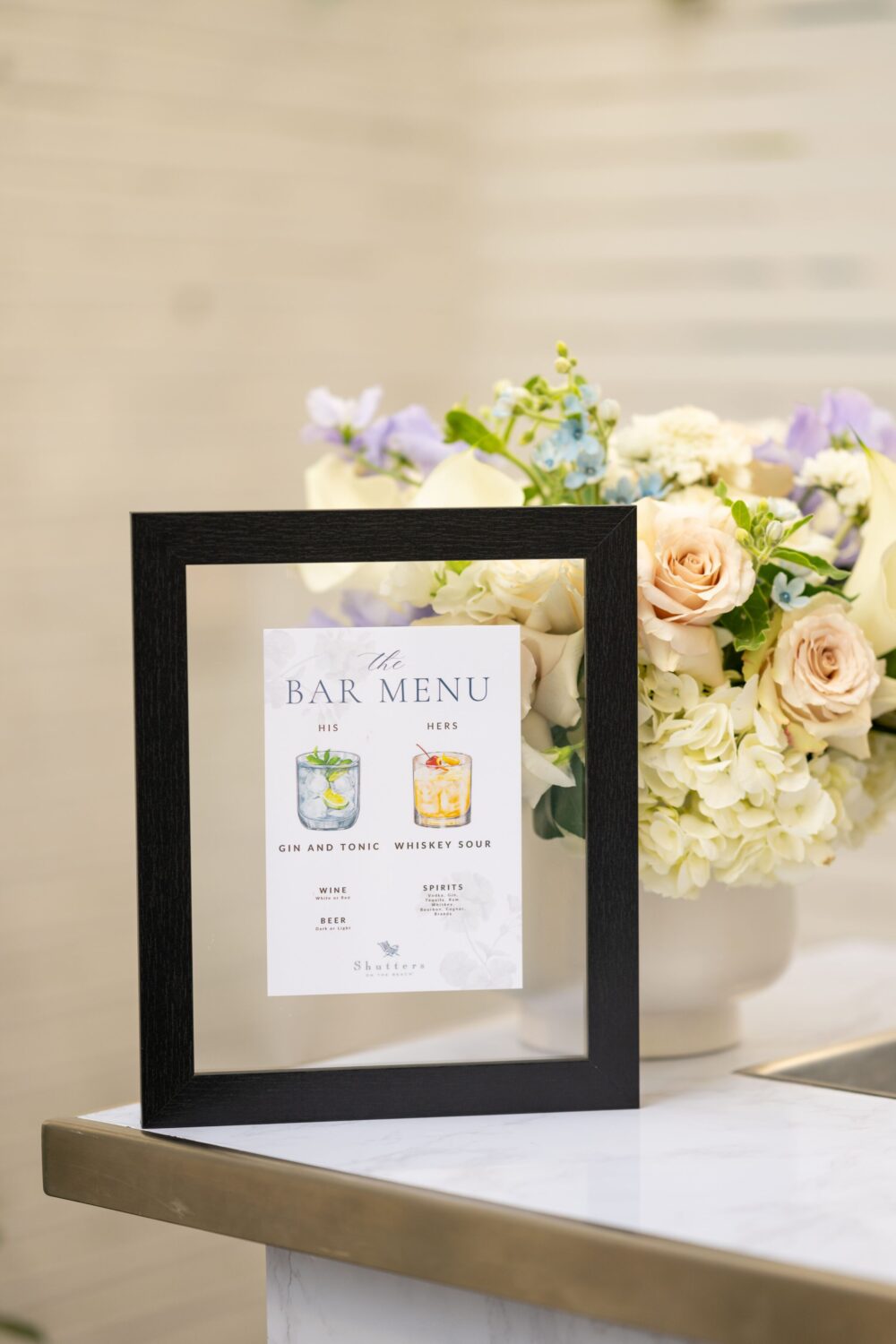 A framed bar menu with drinks options and a floral arrangement in the background.