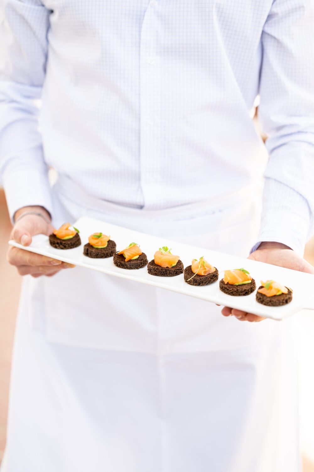 Elegant waiter serving smoked salmon canapés on rye toast, garnished with herbs.