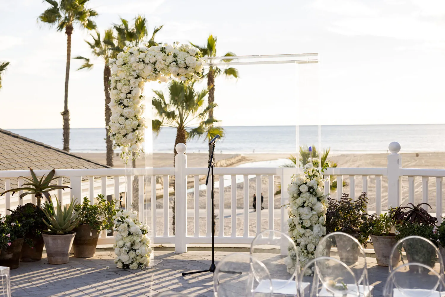 Elegant beachside wedding altar with white floral arrangements, a clear arch, and ocean views.