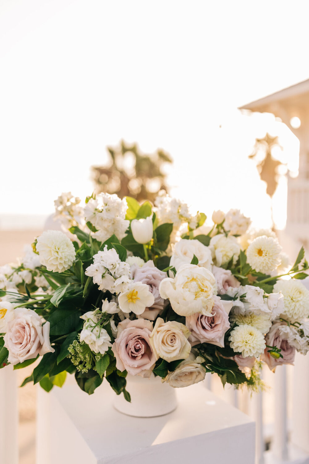 Elegant floral arrangement with pastel roses, white dahlias, and lush greenery in soft sunlight.