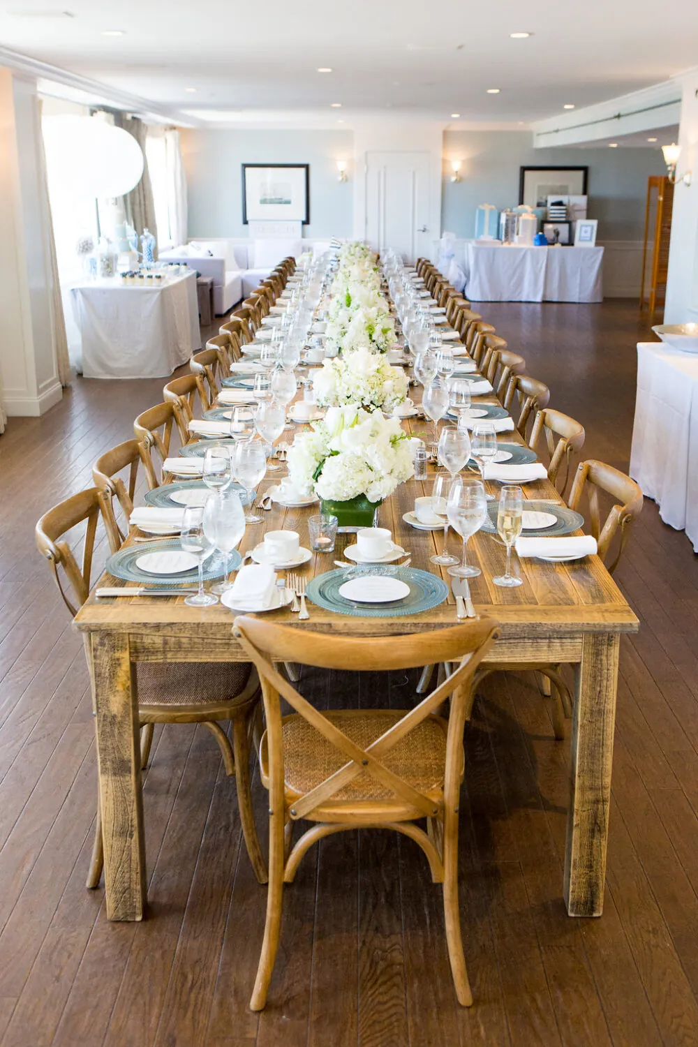 Elegant event setup with a long rustic dining table, white floral centerpieces, and fine tableware.