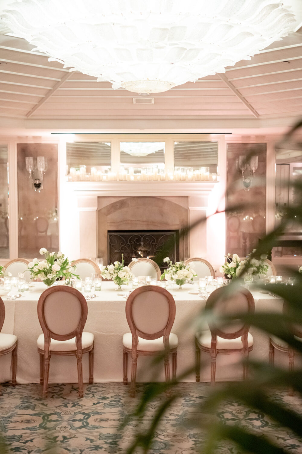 Elegant candlelit dining setup with floral arrangements, a cozy fireplace, and a grand chandelier.