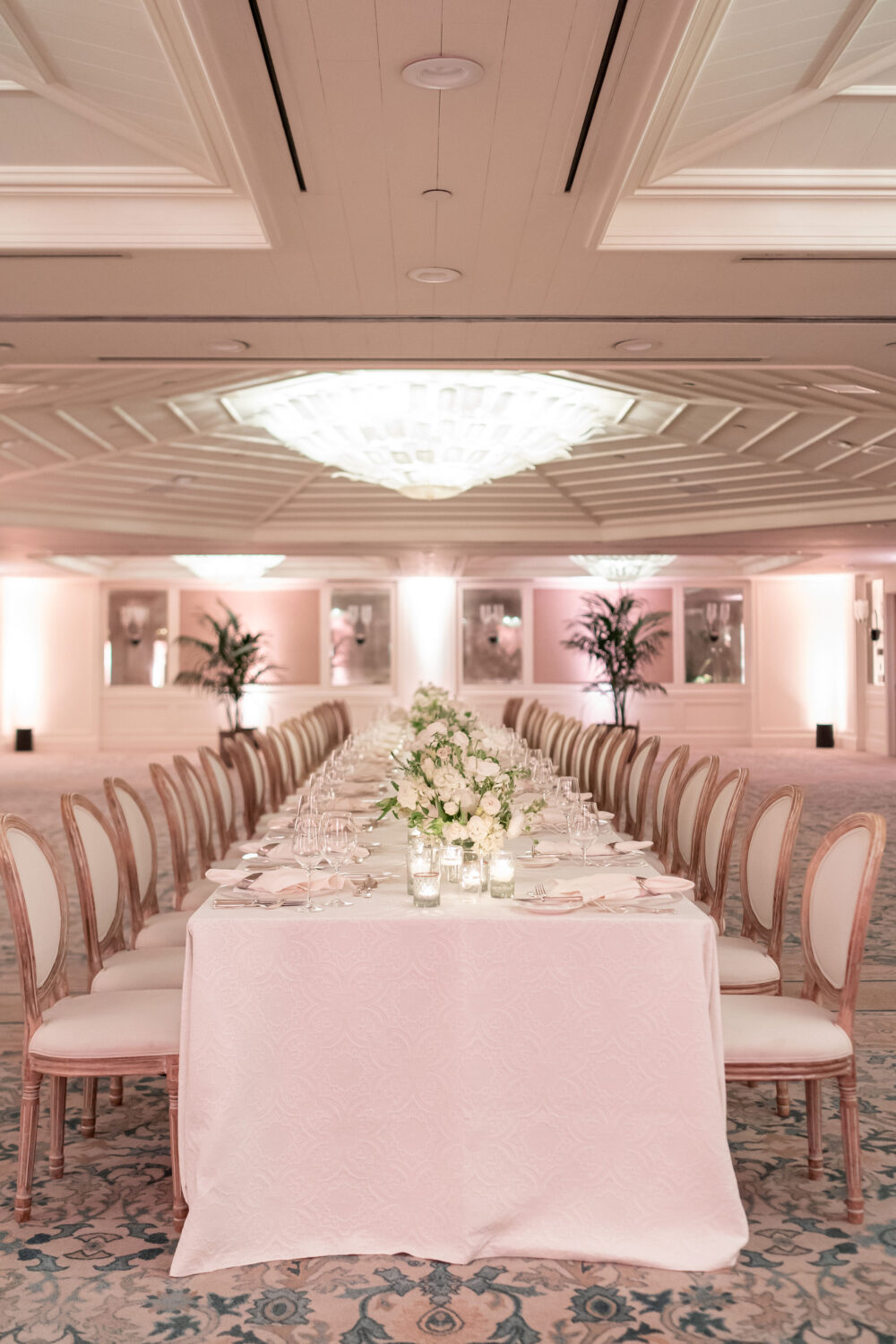 A beautifully set long dining table adorned with white flowers and candles under soft lighting.