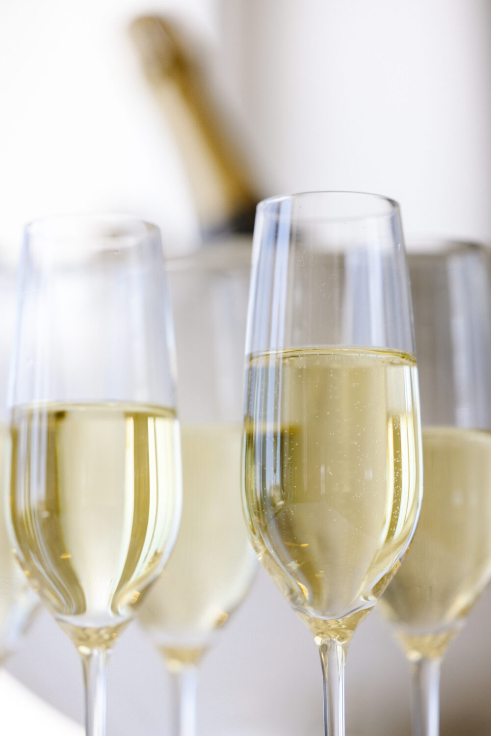 Close-up of champagne glasses with bubbles, with a bottle in the background.