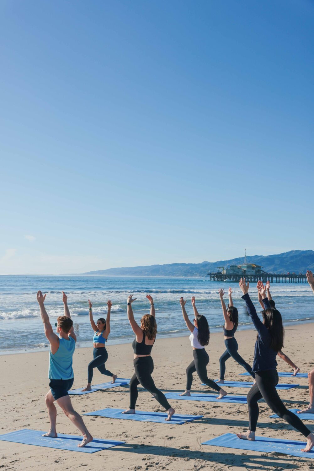 people in warrior one pose on the beach looking at the ocean
