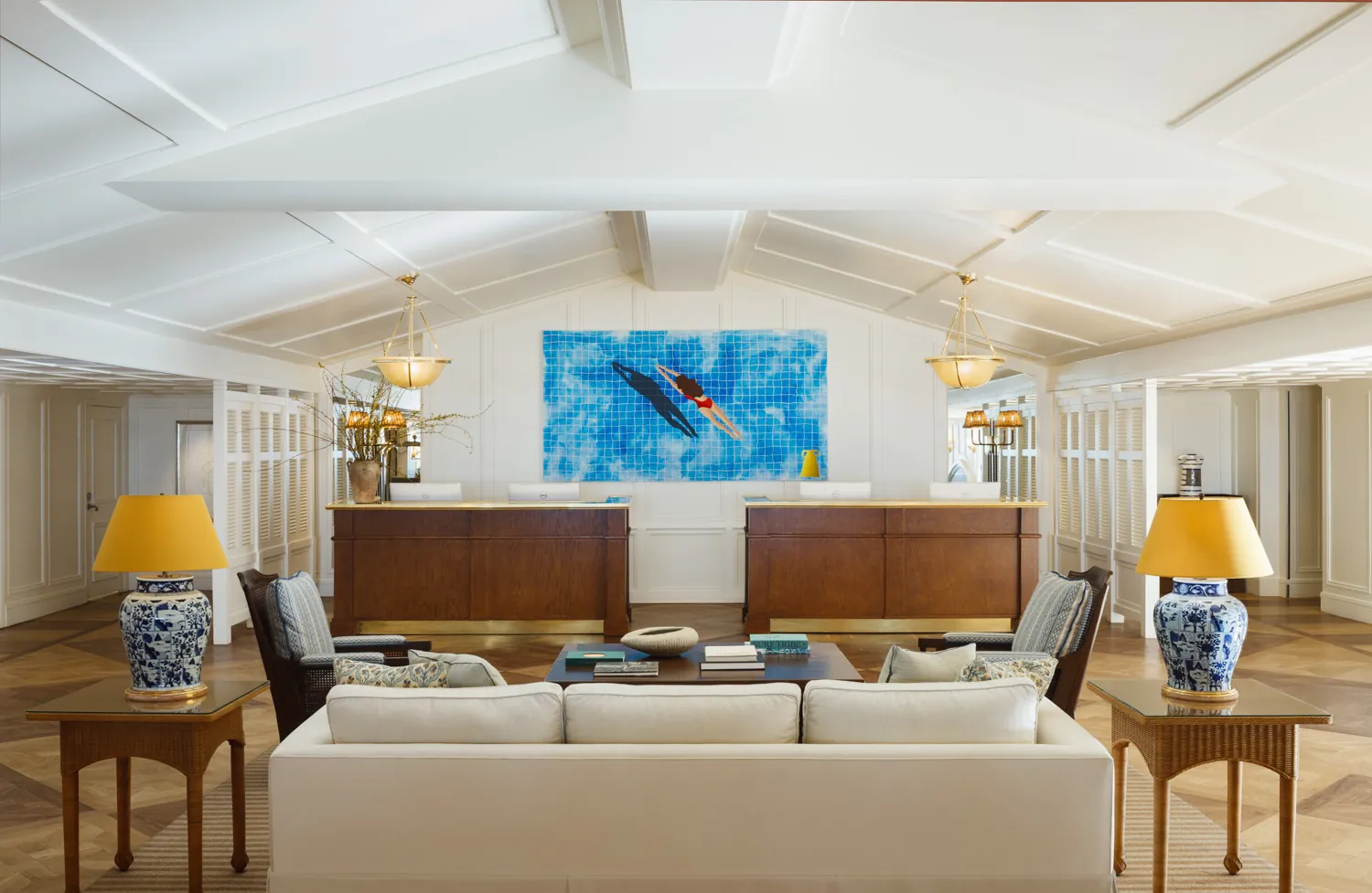 Elegant lounge area with a white sofa, wooden tables, and a large painting of a swimmer on the wall.