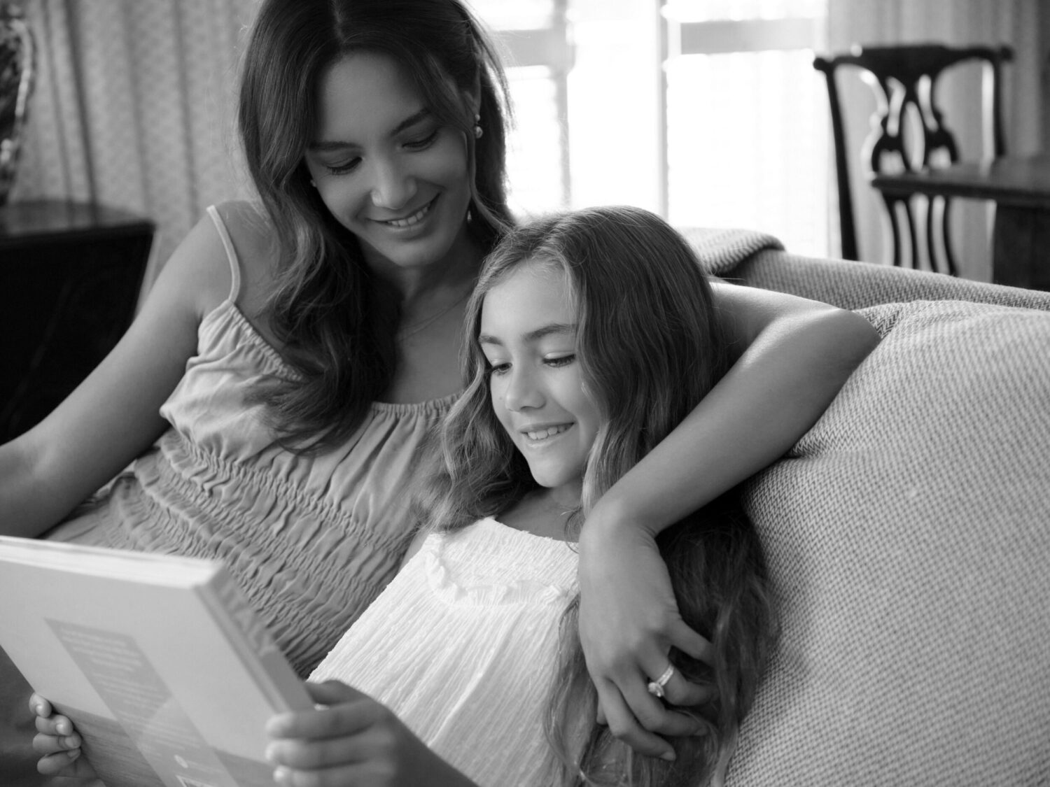 Mother and daughter sitting together on a couch, smiling and looking at a book.