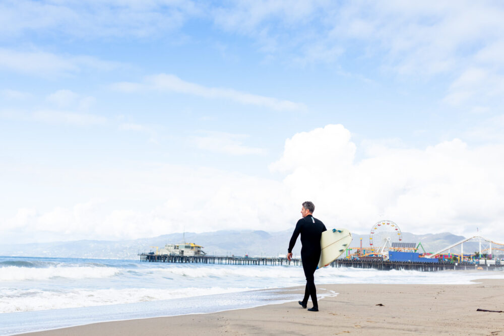 man in a wetsuit, holding a surfboard walking towards the ocean