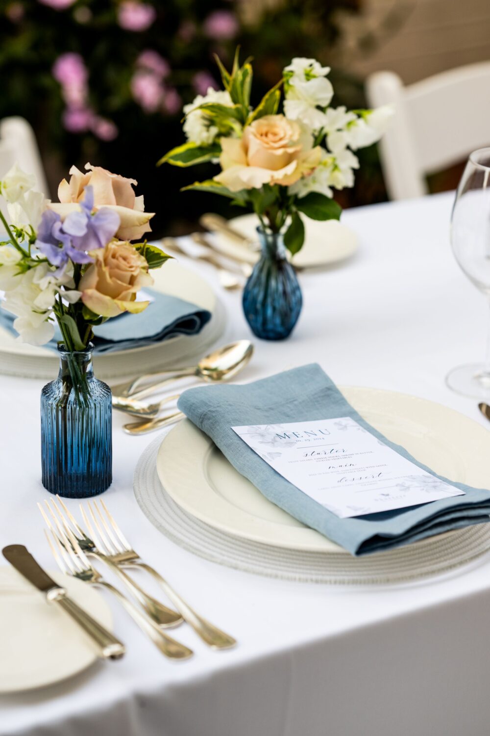 Elegant table with gold flatware, blue napkins, flowers, and a printed menu for a formal event.