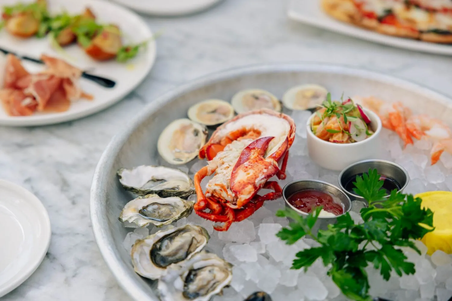 Fresh seafood platter with lobster, oysters, shrimp, and sauces served on crushed ice.