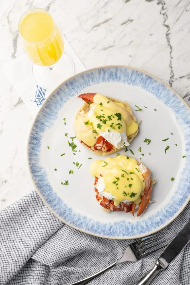 Lobster eggs Benedict on a plate with a mimosa in the background.