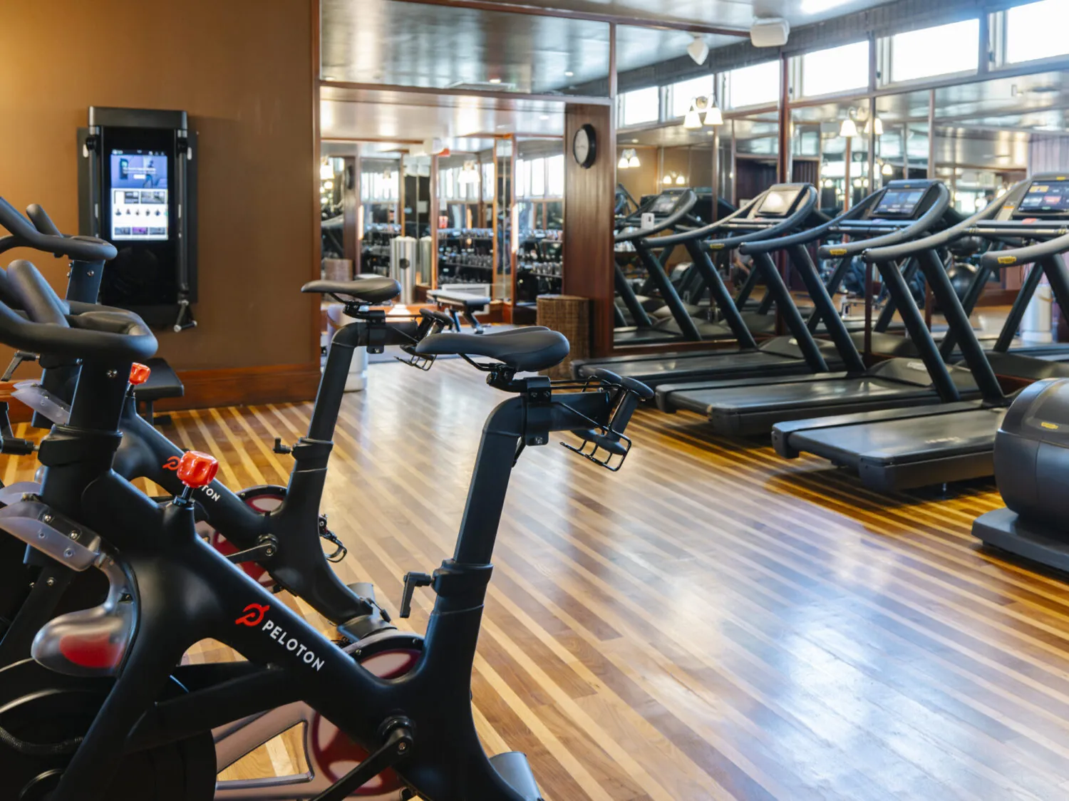 Modern gym with Peloton bikes, treadmills, and mirrored walls reflecting fitness equipment.