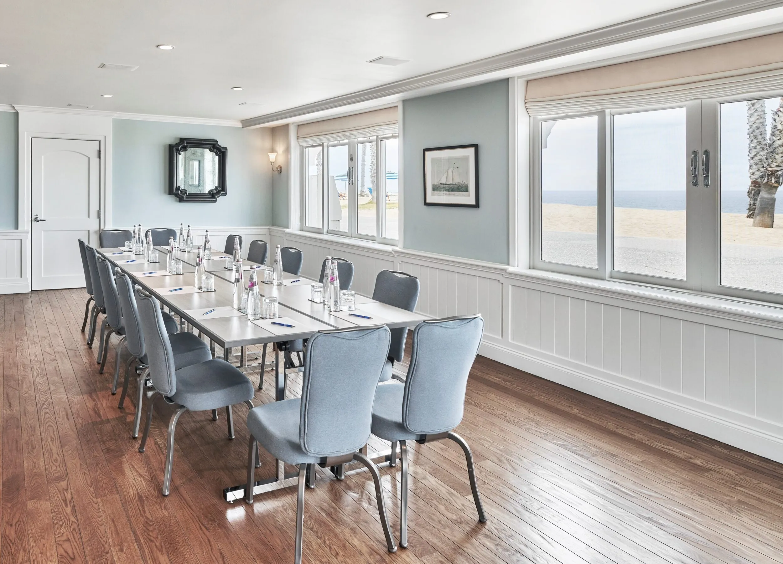 Conference room with ocean views, blue chairs, and a meeting table set with water and notepads.