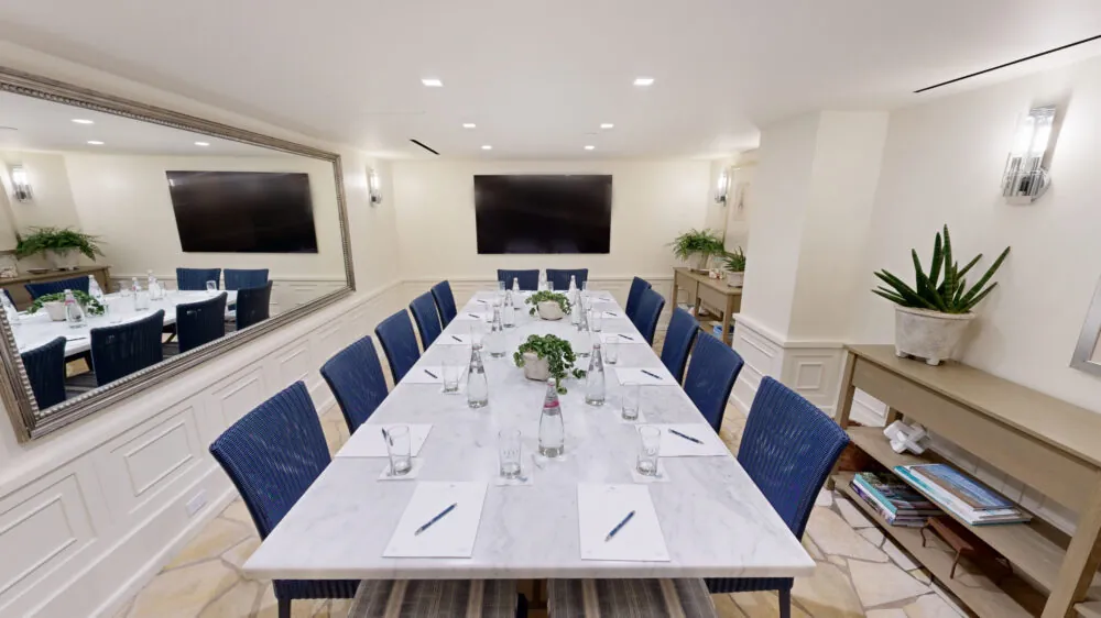 Modern conference room with a marble table, blue chairs, and two large screens.