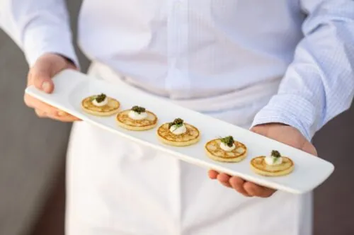 Elegant bite-sized blinis with caviar and cream, served on a sleek white platter.
