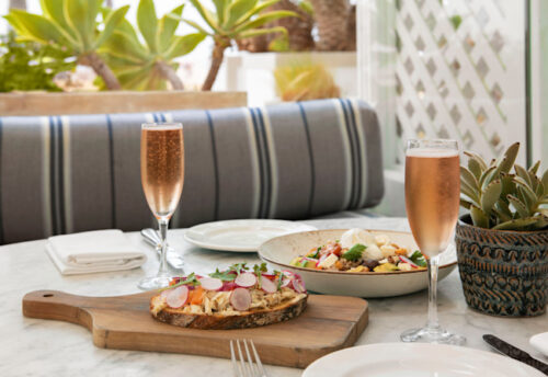 Outdoor table with bruschetta, salad, and two glasses of champagne.