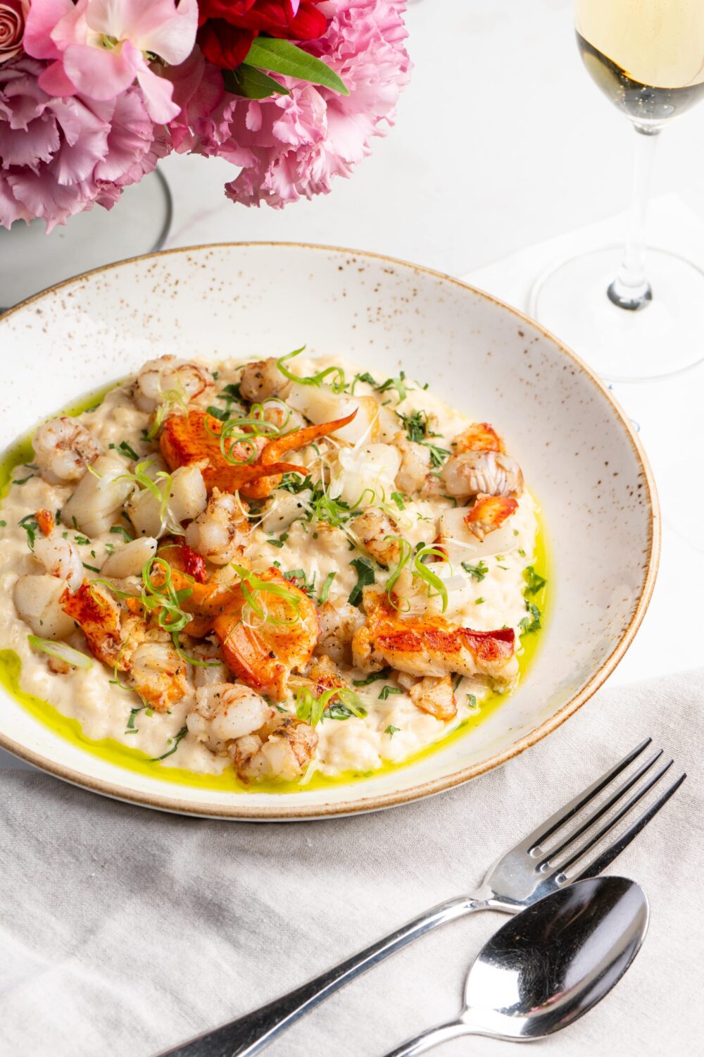 A plate of gnocchi with lobster, garnished with herbs and sauce, on a white table.