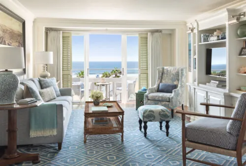 Coastal living room with ocean views, blue decor, plush seating, and a balcony with white chairs.