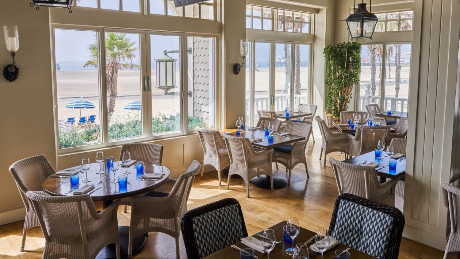 A beachside restaurant with a view of the ocean, tables set with blue glasses.