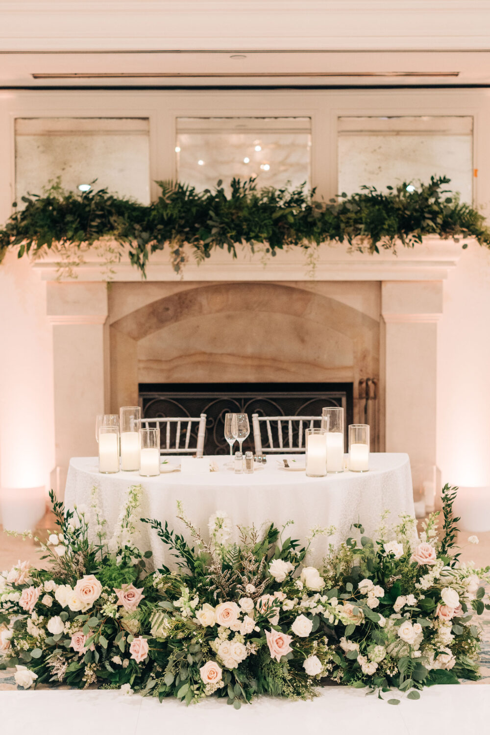 Romantic wedding sweetheart table with candles, floral arrangements, and a fireplace backdrop.