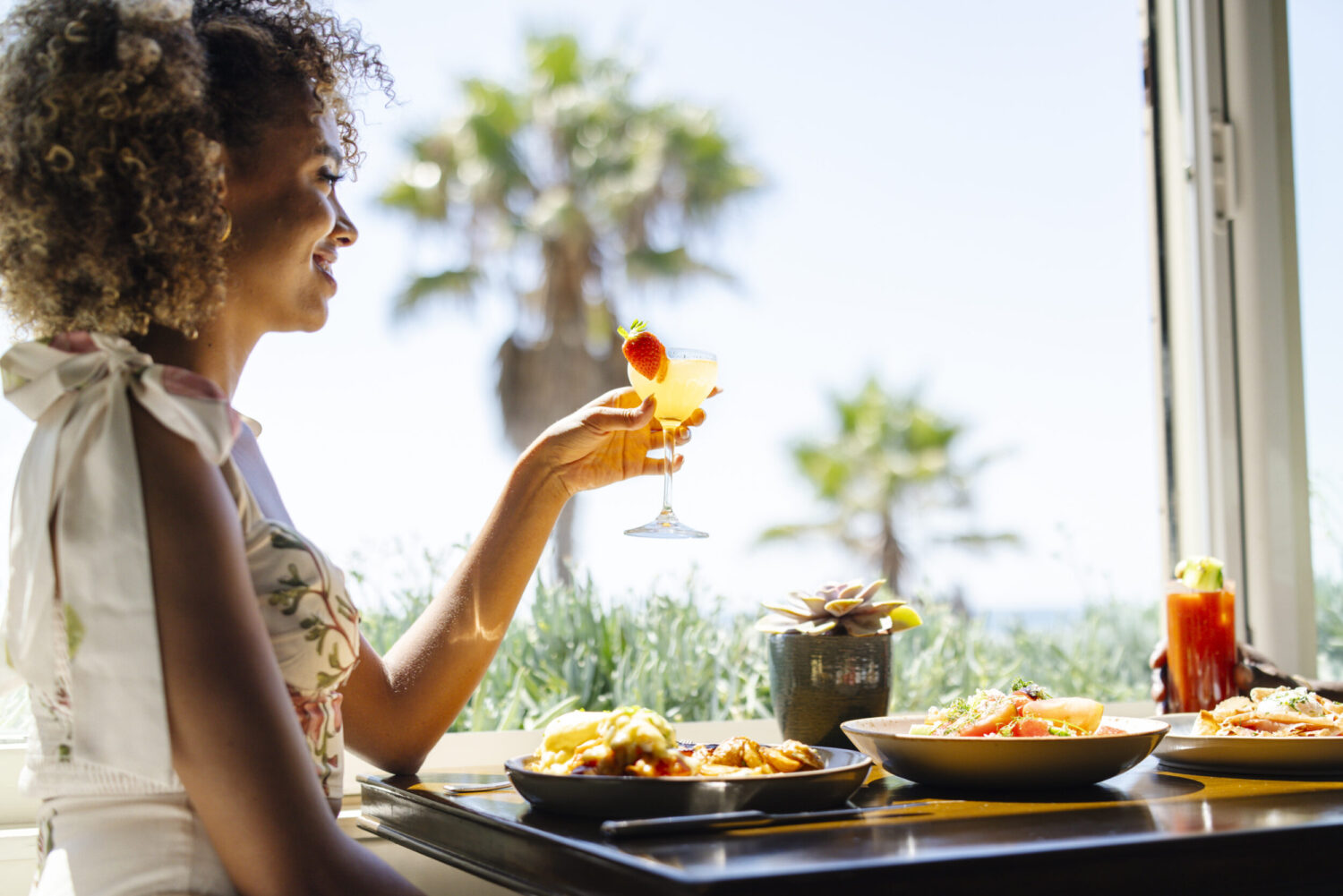 A woman smiles and holds up her cocktail at brunch