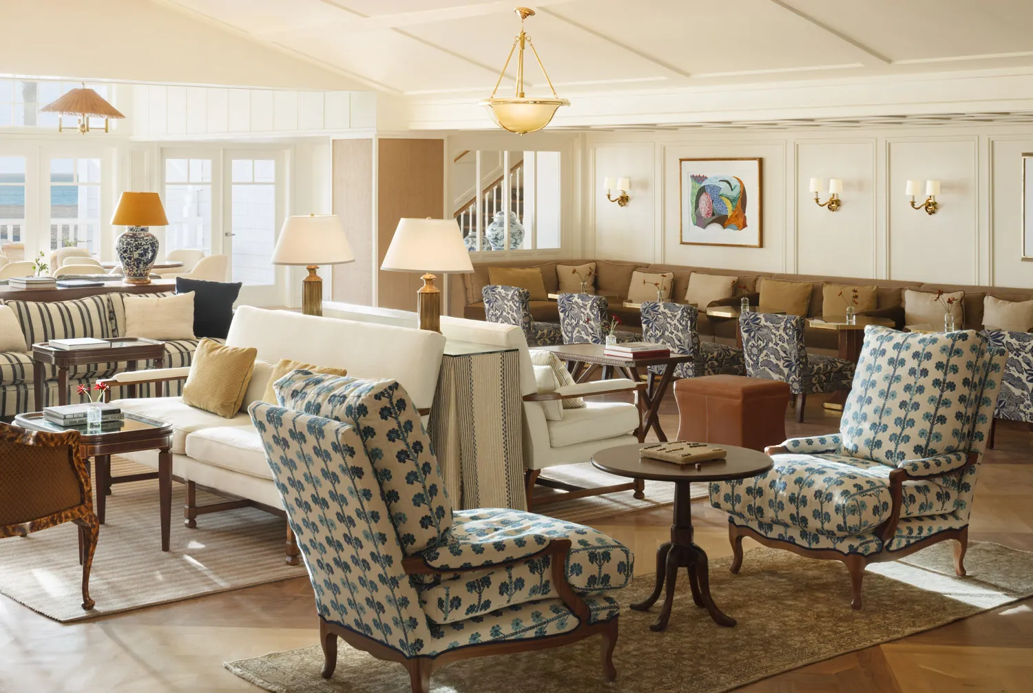 Bright, spacious lounge with floral-patterned armchairs and large windows overlooking the ocean.
