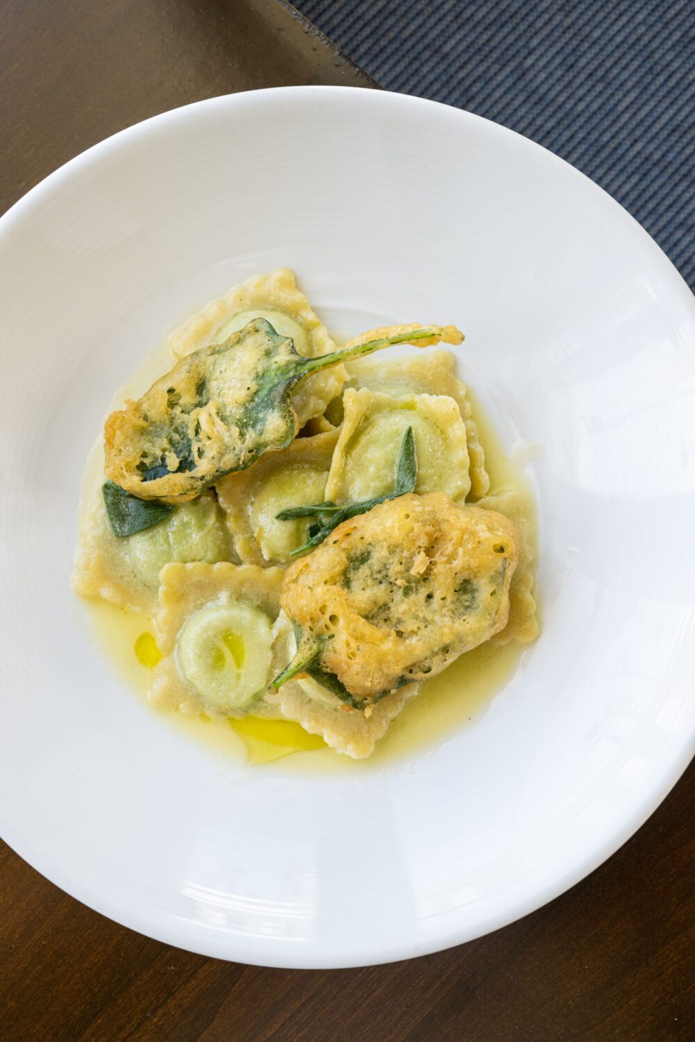 Homemade ravioli in a light cream sauce, garnished with sage leaves and a drizzle of olive oil.