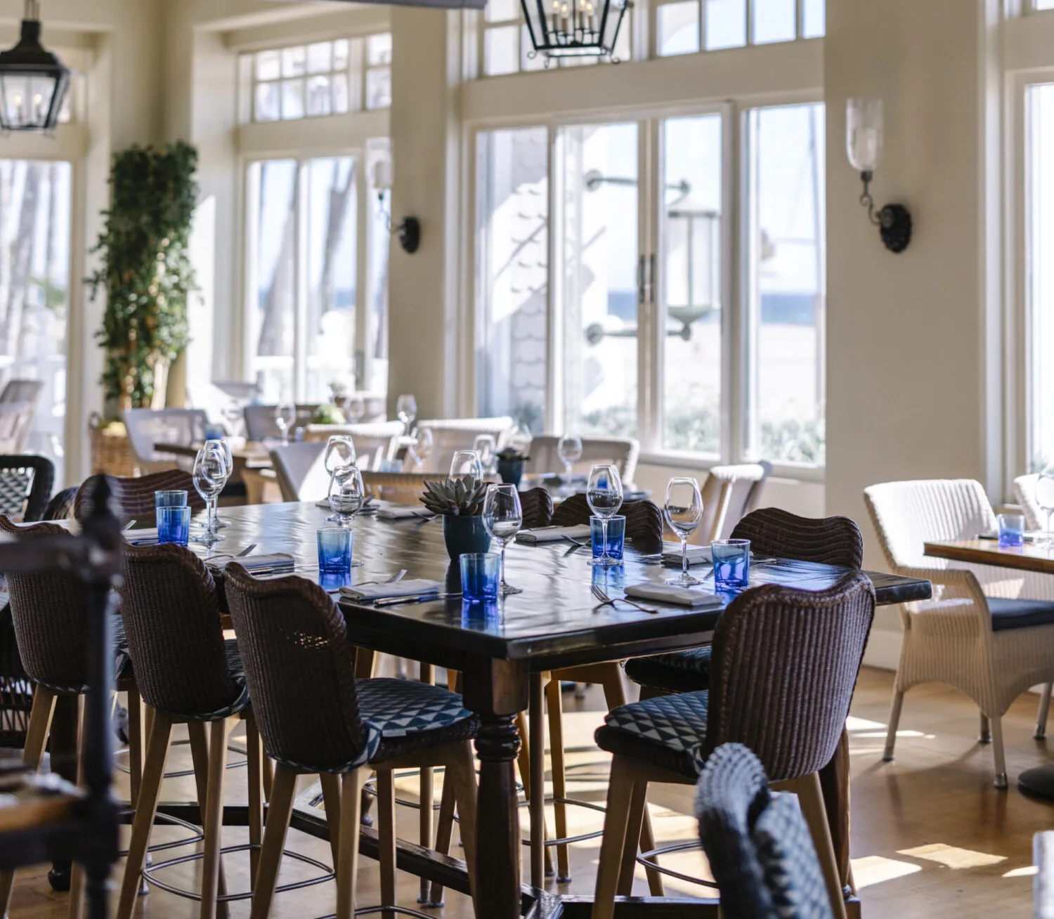 1 Pico restaurant with large windows, wicker chairs, and tables set with wine glasses.