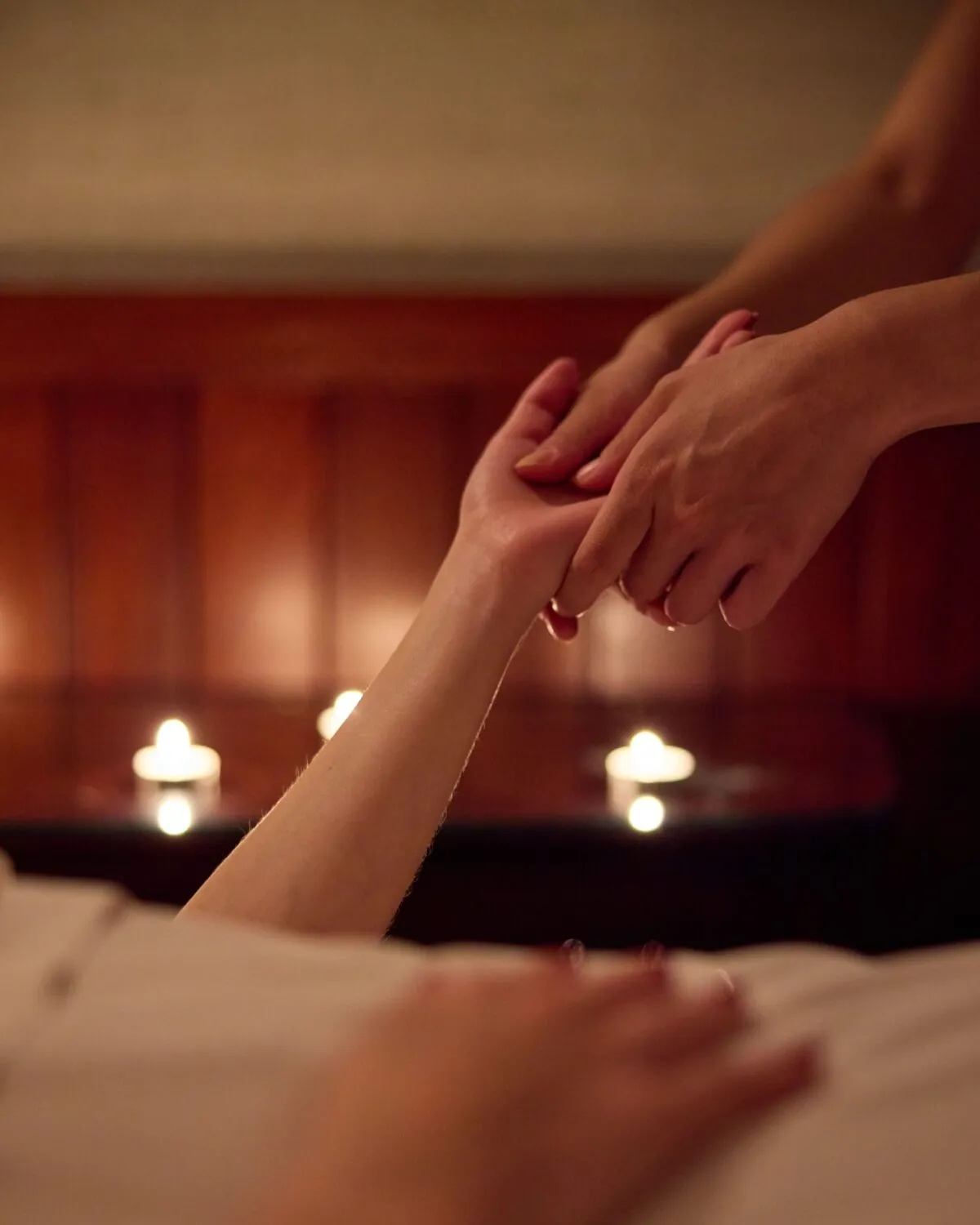 Close-up of hands during a massage, with candles in the background creating a calming atmosphere.