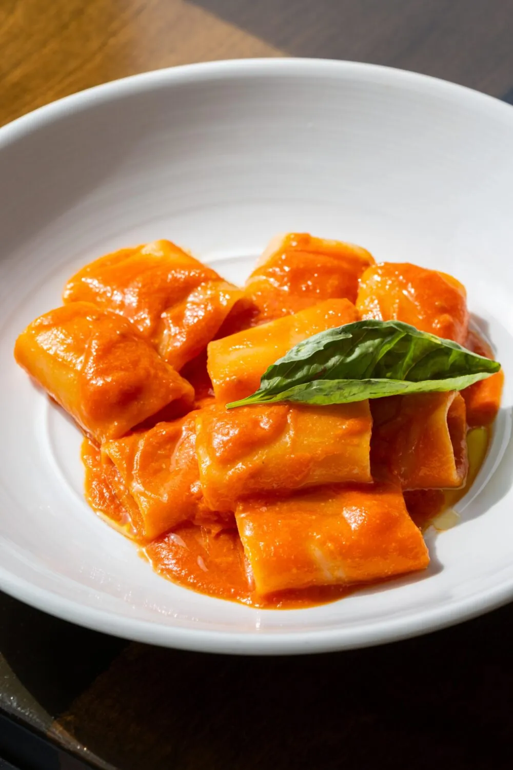 A plate of cannelloni pasta covered in vibrant red tomato sauce, garnished with a basil leaf.