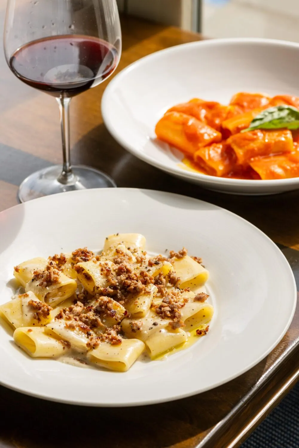 Plate of creamy pasta paired with red wine and a side of tomato pasta.
