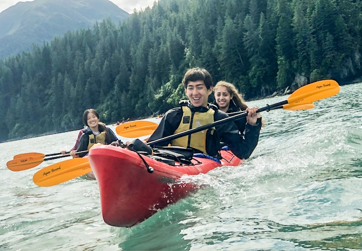 Happy teen travelers kayaking on an adventure trip