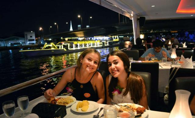 Teenage travelers enjoy local cuisine on riverboat cruise during summer youth travel program in Thailand
