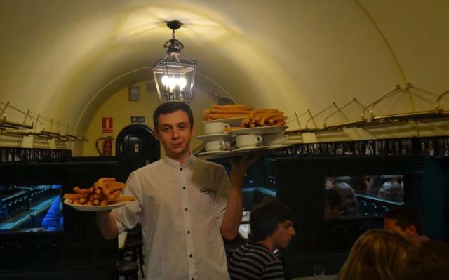 Waiter at churreria San Gines in Madrid carries churros and chocolate to teens on summer youth travel program