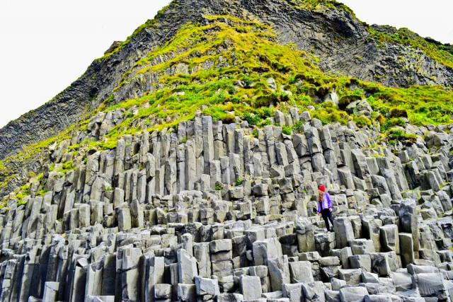 Teen with basalt rock formations in Iceland on summer adventure travel program