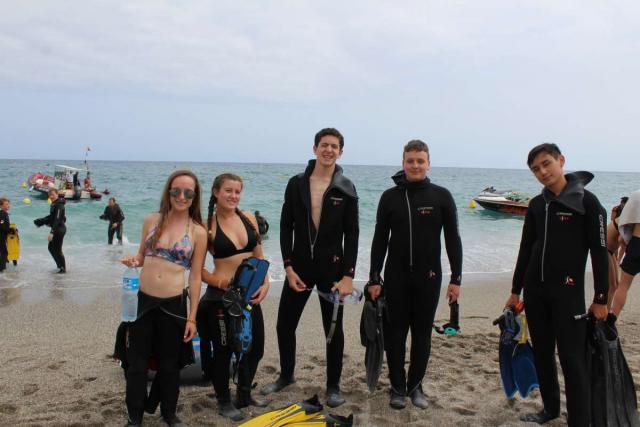 Teenage travelers on beach in wetsuits about to go scuba diving in Malaga on summer youth adventure program