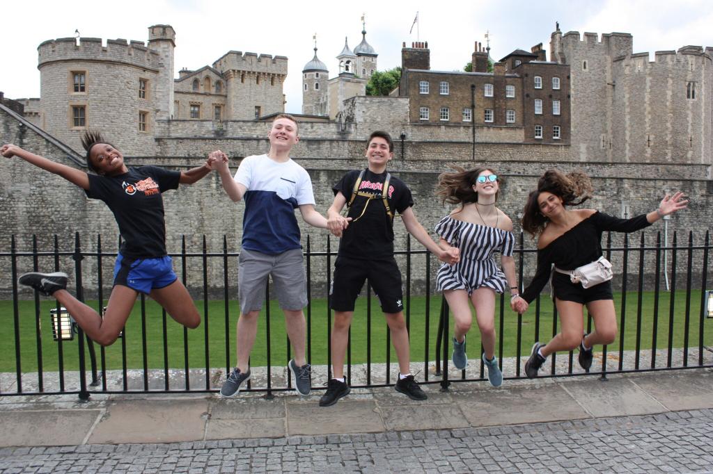 Happy teen travelers jump at Tower of London on summer travel program in England