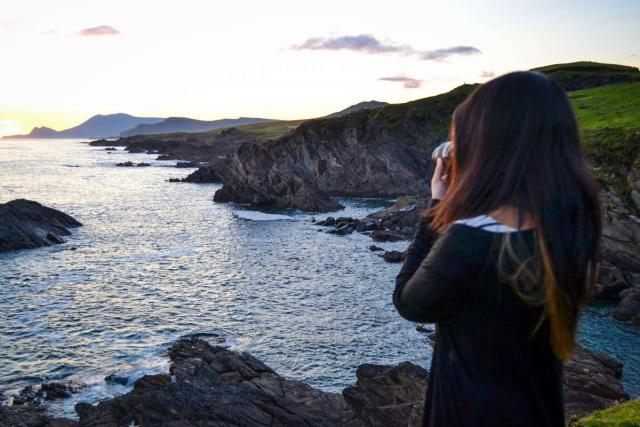 Teenage traveler photographs sunset over Irish cliffs during summer teen travel program