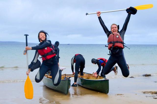 Teen travelers sea canoeing and happy jumping during summer youth adventure travel program in Ireland
