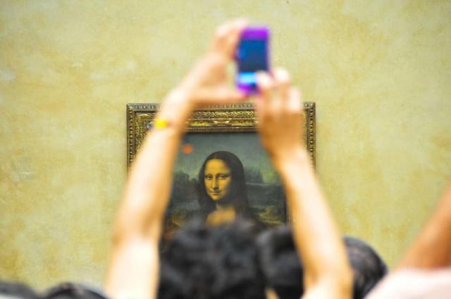 Teenage traveler photographing Mona Lisa at Louvre Museum in Paris during summer French language immersion program