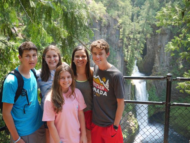 A group of teens takes a photo at a waterfall during their summer travel program in North America.