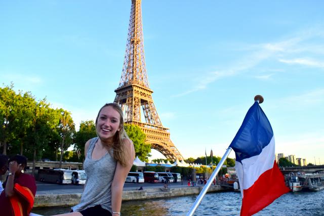 Teenage traveler on Seine river cruise with French flag and Eiffel Tower on summer travel photography program
