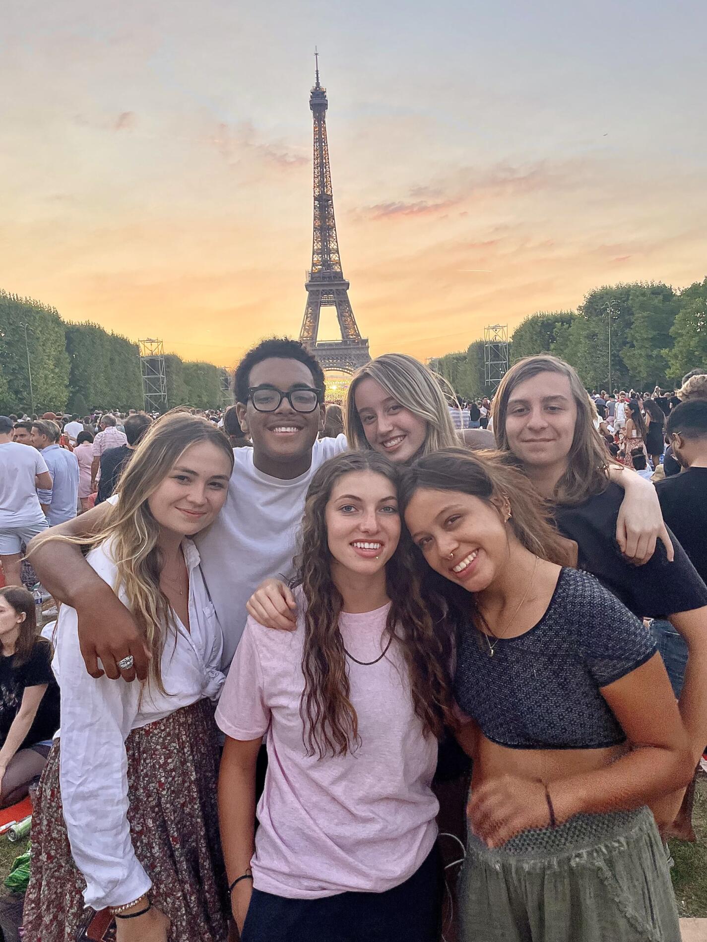 A group of teens on a summer tour of Europe posing in front of the Eiffel Tower at sunset