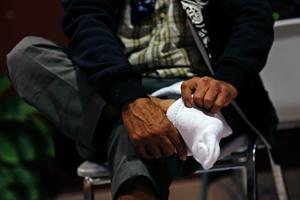Homeless man removes sock to prepare for feet washing