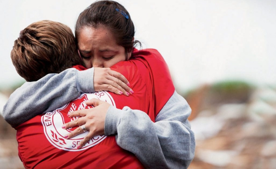 Salvation Army disaster relief volunteer hugs woman during humanitarian response.